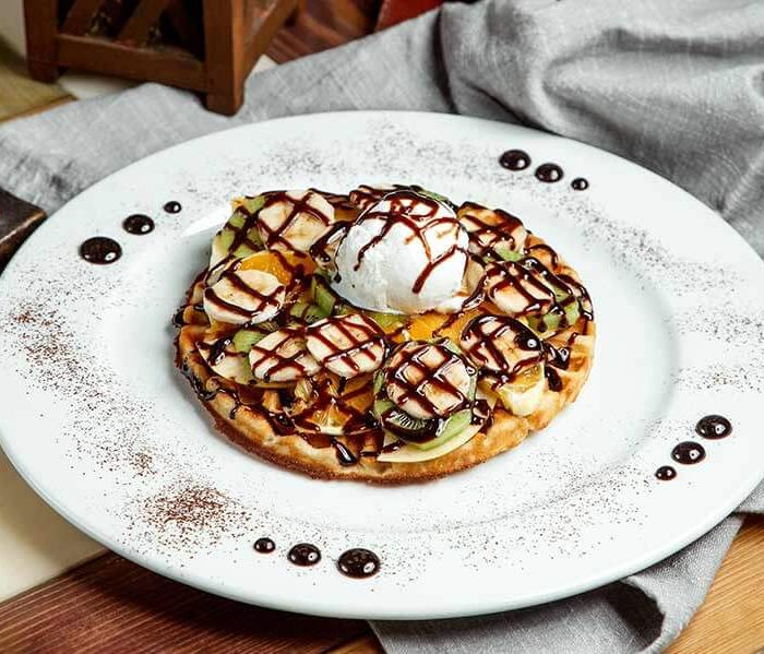 Waffle with ice cream scoops, fruits and chocolate