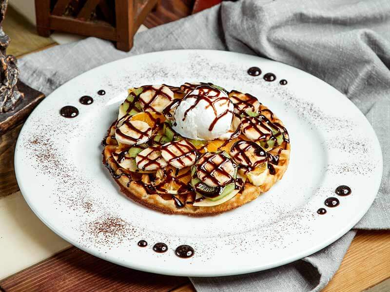 Waffle with ice cream scoops, fruits and chocolate